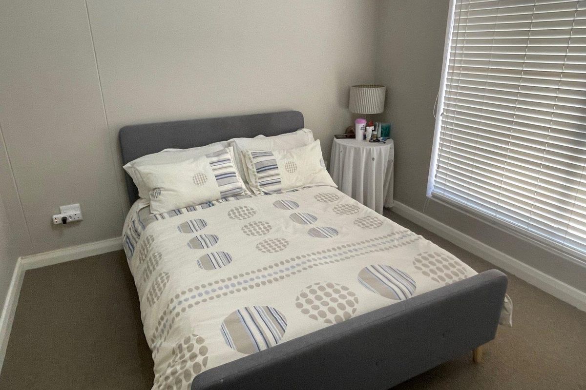 A functional bedroom featuring neutral wall tones, carpeted flooring, and venetian blinds for adjustable natural light control.