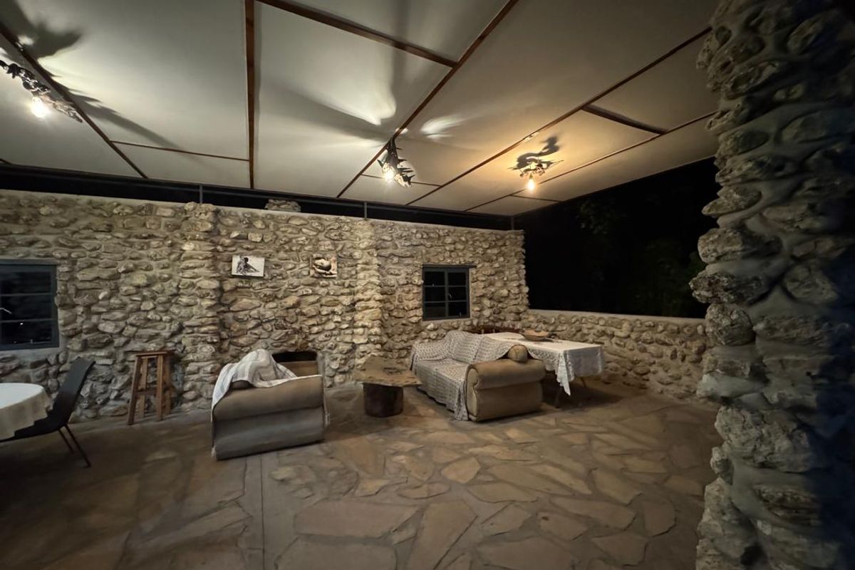 Spacious covered outdoor patio featuring rustic stone masonry walls, flagstone flooring, and exposed beam ceiling, ideal for evening entertainment.