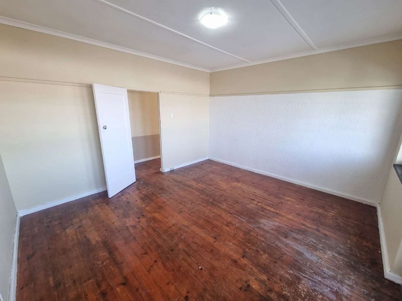 An empty bedroom featuring original hardwood flooring, neutral wall tones, and a classic picture rail, offering a blank canvas for renovation.