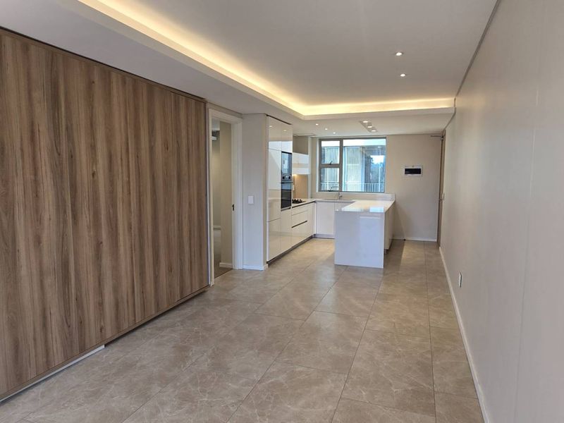 Modern open-plan living and kitchen area featuring sleek built-in cabinetry, a central kitchen island, recessed lighting, and neutral tiled flooring throughout.