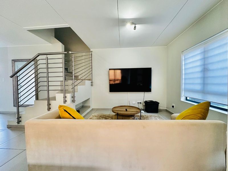 Modern living room featuring tiled flooring, a sleek stainless steel staircase railing, and neutral wall finishes with integrated lighting.