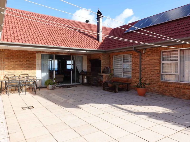 Spacious paved patio area featuring a built-in braai, brick exterior walls, and direct access to the interior living space through sliding glass doors.