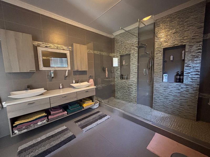 Modern bathroom featuring a double vanity with vessel sinks, a spacious walk-in shower with mosaic tile accents, and built-in storage niches.