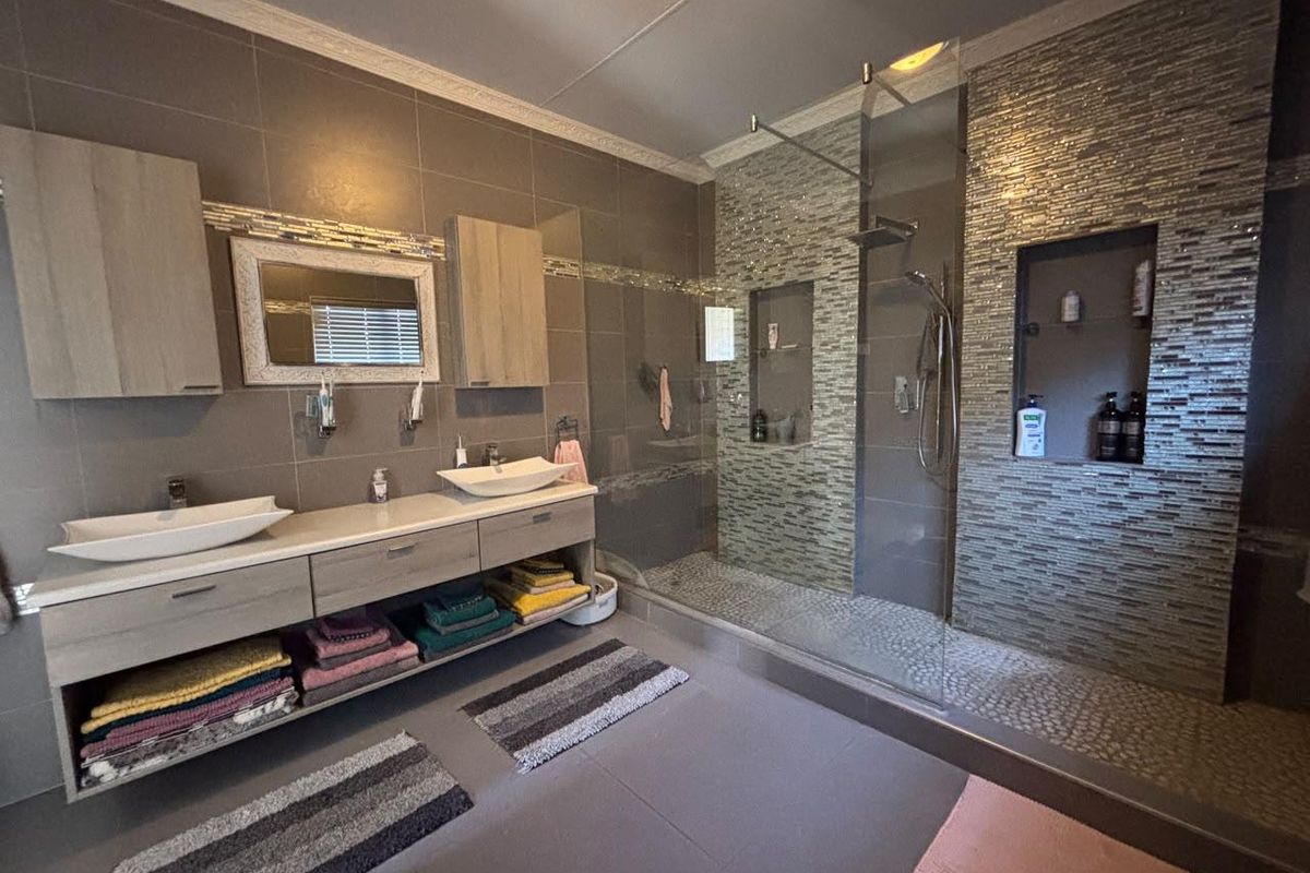 Modern bathroom featuring a double vanity with vessel sinks, a spacious walk-in shower with mosaic tile accents, and built-in storage niches.