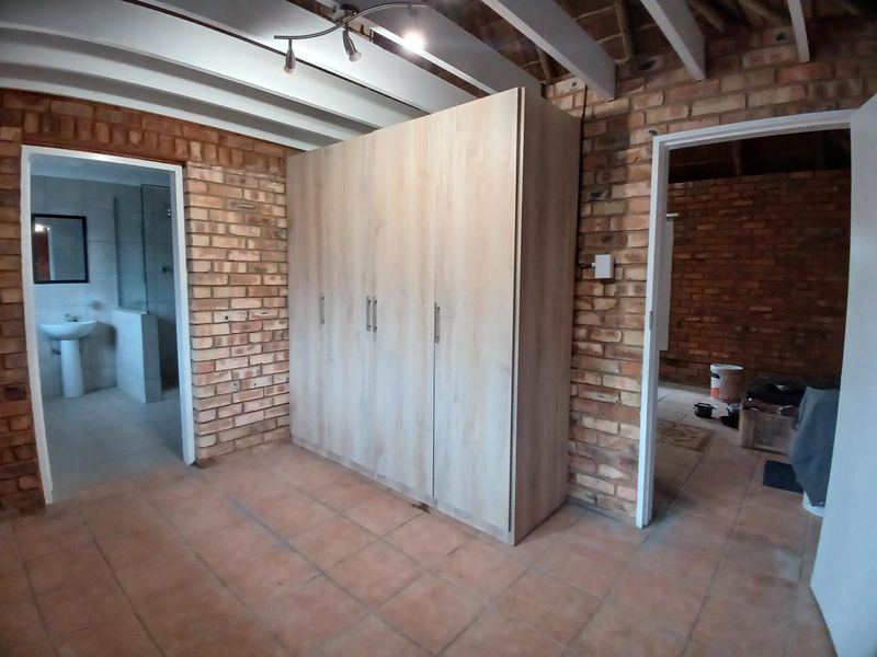 Bedroom featuring exposed brick walls, timber ceiling beams, tiled flooring, and a built-in wardrobe, with an adjoining en-suite bathroom.