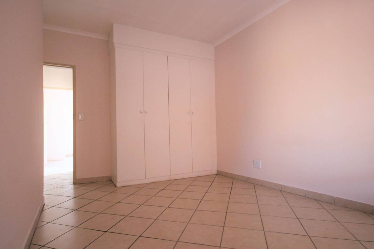 An empty bedroom featuring neutral wall paint, tiled flooring, and built-in cupboards, offering a clean and versatile space ready for personalization.