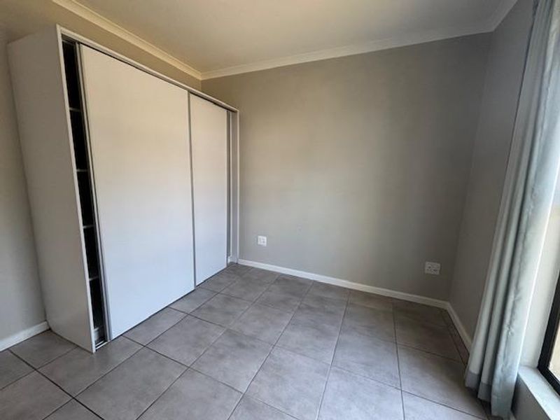 A clean, empty bedroom featuring neutral grey wall paint, large format floor tiles, and a modern built-in sliding door wardrobe.