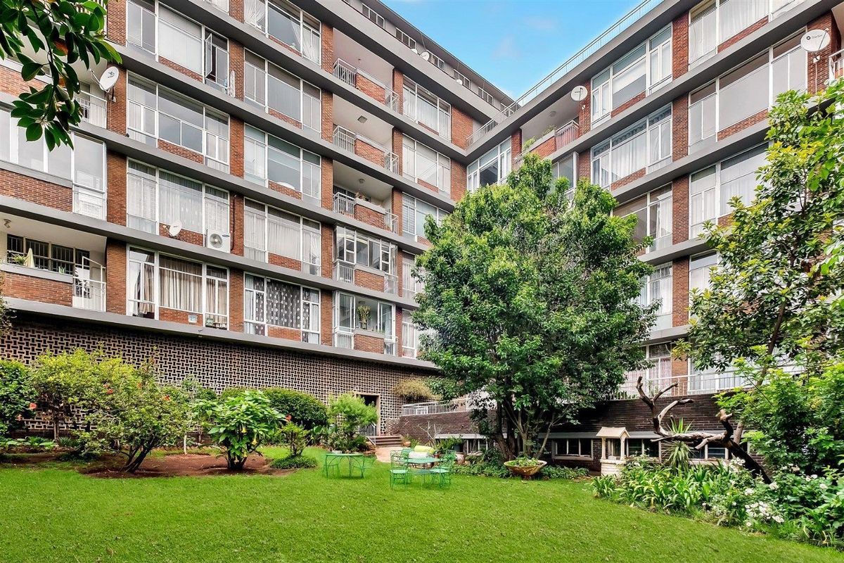 A view of the apartment building facade overlooking a shared garden area with mature trees and lawn.