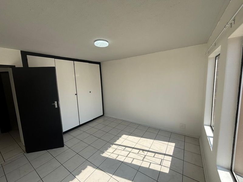 A bright, empty bedroom featuring neutral tiled flooring, built-in cupboards with contrasting trim, and natural light from the side window.
