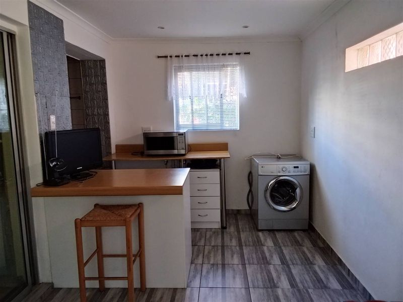 A functional kitchen area featuring tiled flooring, built-in cabinetry with laminate countertops, and a dedicated space for laundry appliances.