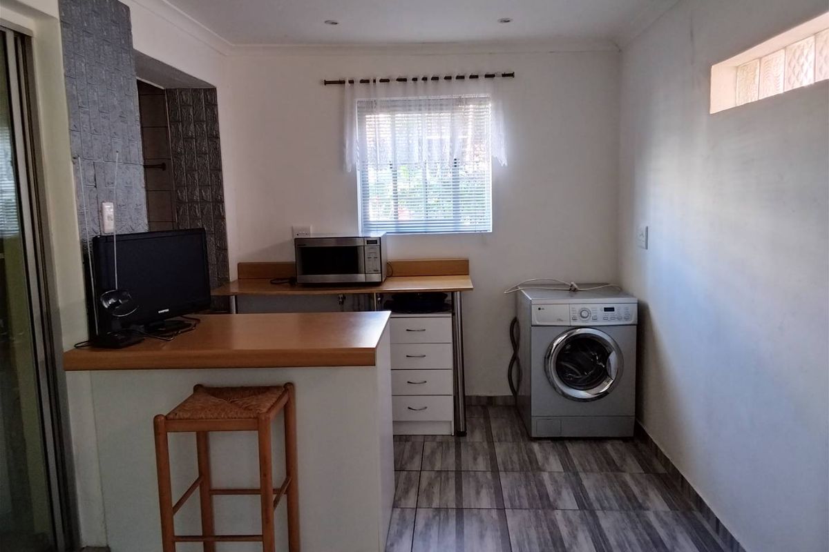 A functional kitchen area featuring tiled flooring, built-in cabinetry with laminate countertops, and a dedicated space for laundry appliances.