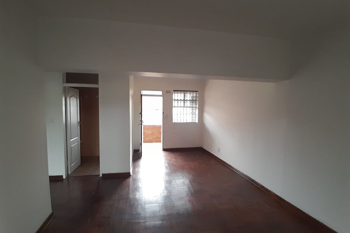 An empty living room featuring dark parquet flooring, neutral walls, and access to an outdoor area through a security gate.