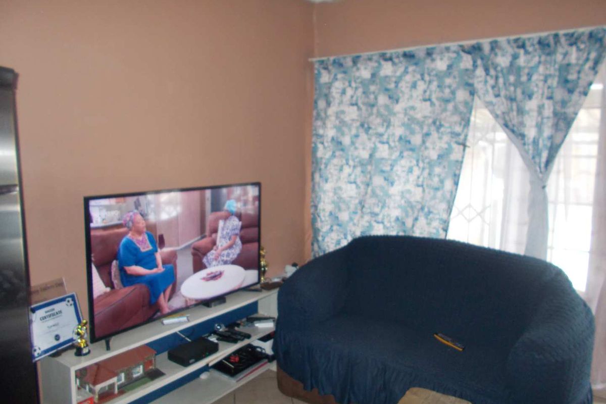 A living room area featuring tiled flooring and a window with security gate, providing a functional space for relaxation.