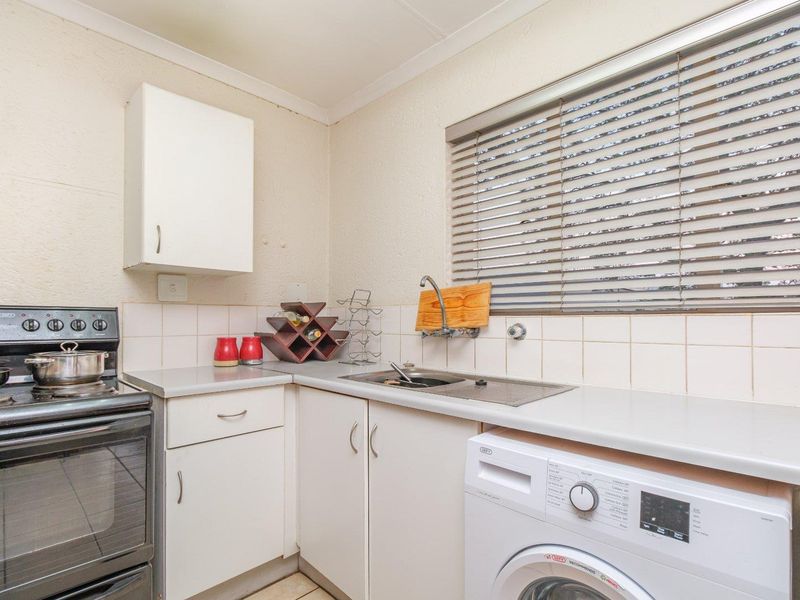 Compact kitchen featuring built-in cabinetry, tiled backsplash, stainless steel sink, and space for a washing machine and freestanding stove.