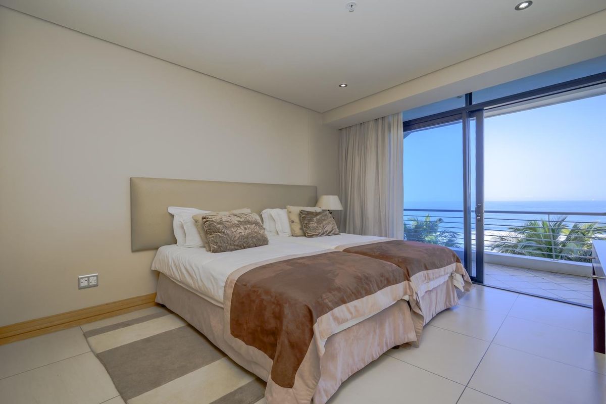 A well-maintained bedroom featuring tiled floors, recessed lighting, and a large sliding glass door providing direct access to a balcony with ocean views.