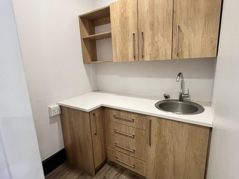 A compact and modern scullery or kitchenette area featuring light wood-finish cabinetry, a white countertop, and a stainless steel sink.
