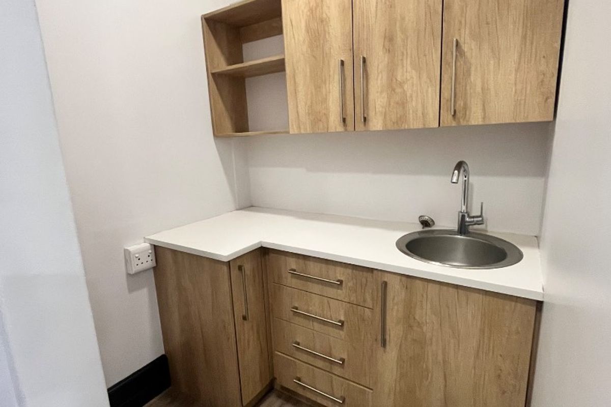 A compact and modern scullery or kitchenette area featuring light wood-finish cabinetry, a white countertop, and a stainless steel sink.