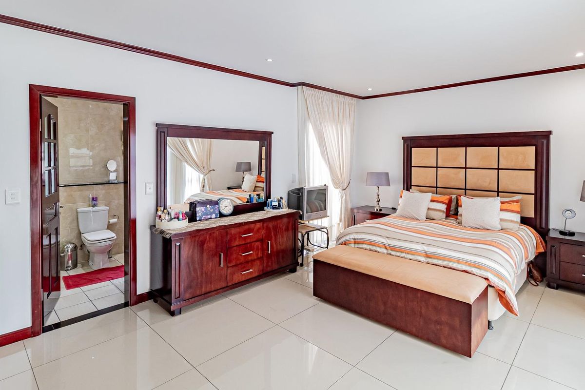 Spacious bedroom featuring tiled flooring, crown molding, and an attached en-suite bathroom with neutral finishes.