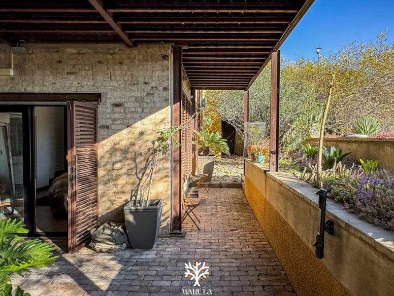 A covered outdoor patio featuring brick paving, an exposed brick wall, and a timber pergola, providing a seamless transition to the garden area.