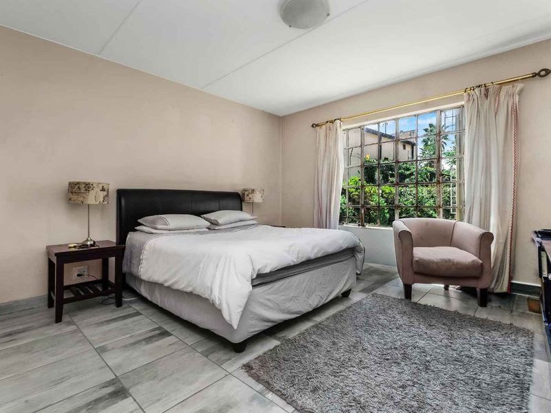 A bedroom featuring tiled flooring and a large window with security bars, offering a view of the exterior greenery.