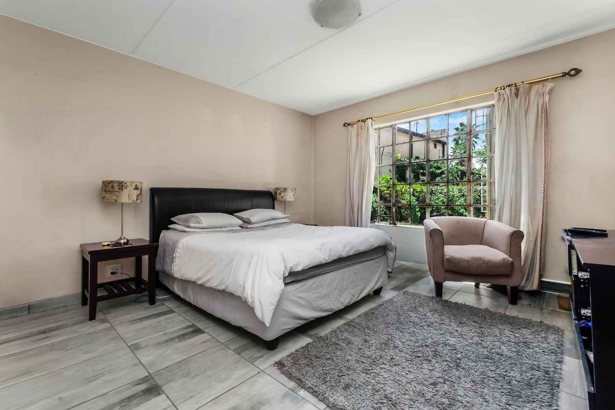 A bedroom featuring tiled flooring and a large window with security bars, offering a view of the exterior greenery.