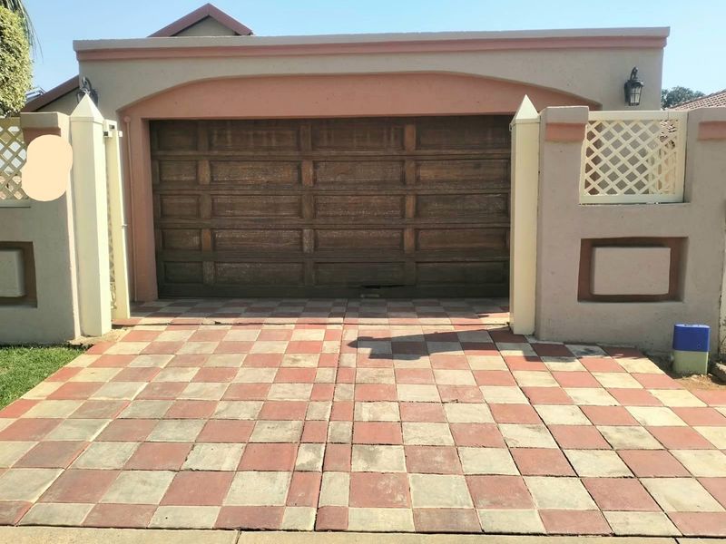 A single garage featuring a wooden sectional door, set behind a paved driveway and masonry boundary wall with decorative lattice detailing.