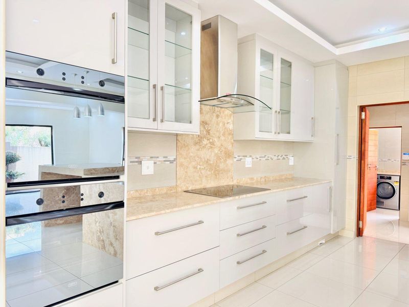 Modern kitchen featuring white cabinetry, stone countertops, built-in oven, induction hob, and a stylish stone-look splashback with recessed lighting.