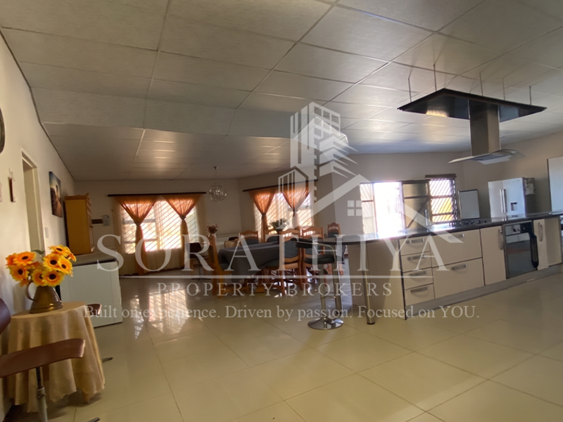 Spacious open-plan living and kitchen area featuring a large central island, modern extractor fan, built-in oven, and neutral tiled flooring throughout.