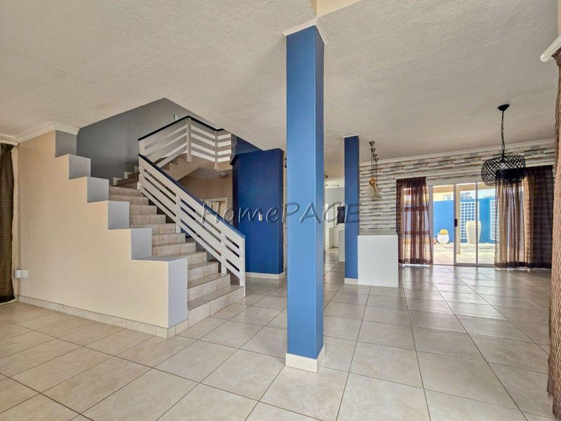 Spacious open-plan living area featuring tiled floors, a central staircase, structural columns, and sliding glass doors leading to the rear outdoor space.