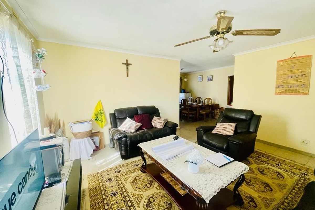 A spacious living room featuring tiled flooring, a ceiling fan, and coving, with an open-plan flow leading towards the dining area.