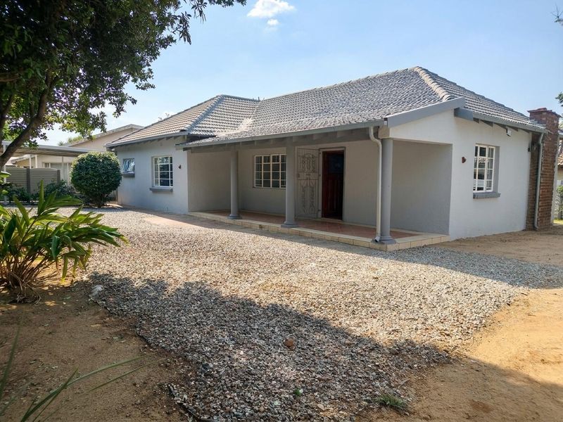 Front view of a single-story house featuring a covered veranda with concrete columns, a tiled roof, and a gravel driveway.