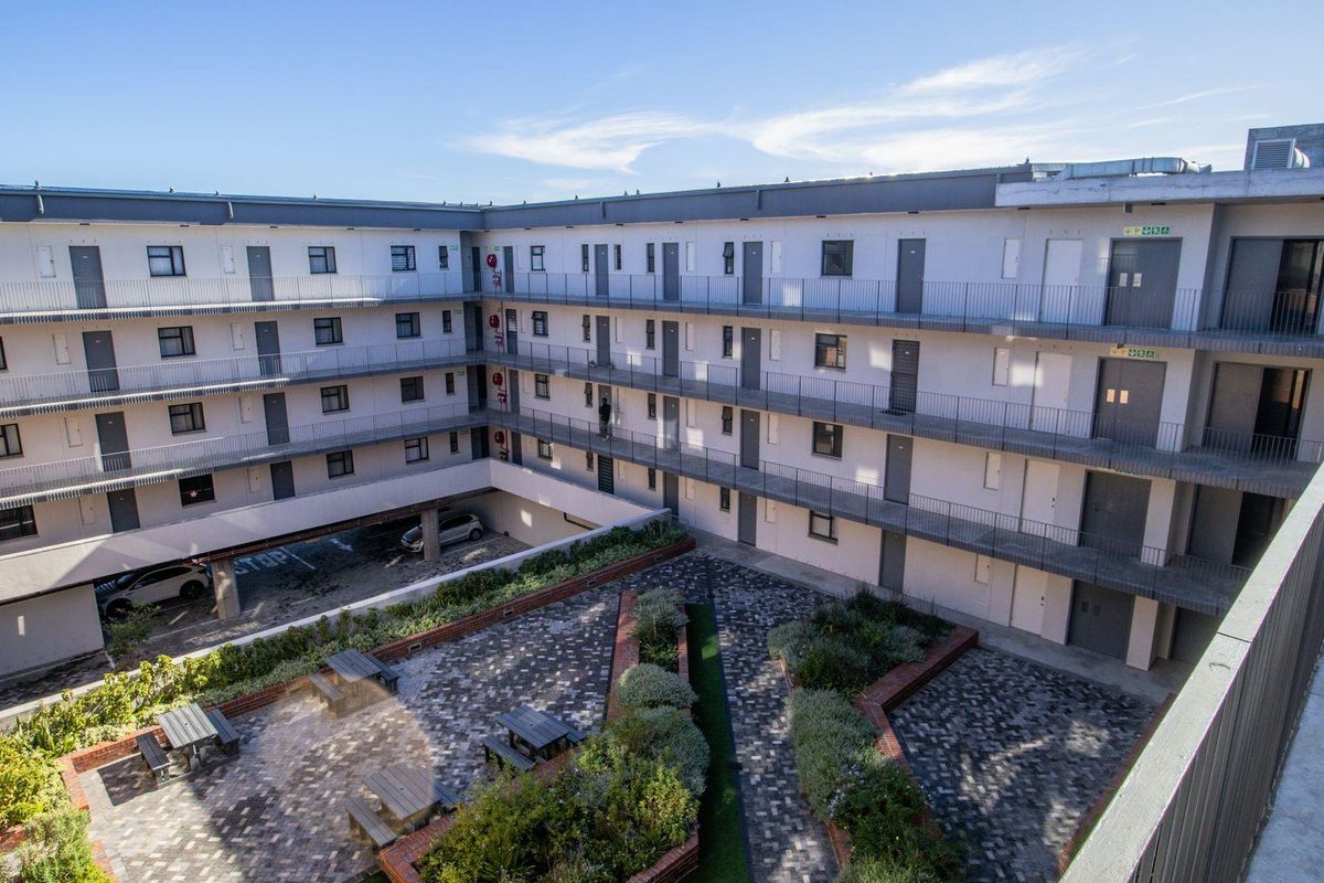An elevated view of an apartment complex courtyard featuring paved walkways, landscaped garden beds, and multi-level access balconies.