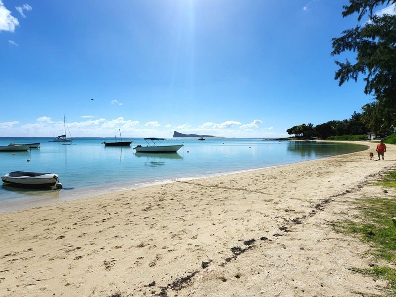 A scenic coastal view featuring a sandy beach, turquoise waters, and moored boats under a clear blue sky.