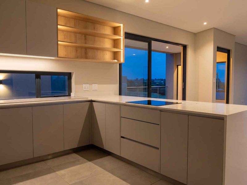 Modern kitchen featuring sleek handleless cabinetry, stone countertops, integrated induction hob, and warm under-cabinet lighting, opening onto an outdoor balcony area.