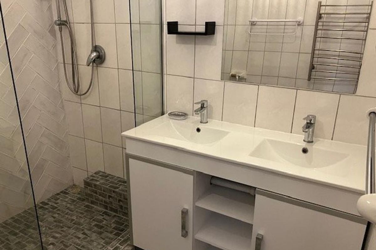 Modern bathroom featuring a double vanity, glass-enclosed shower with herringbone tiling, and a heated towel rail.