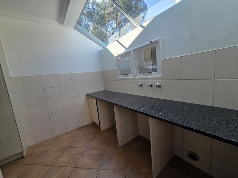 A functional laundry area featuring a granite countertop, tiled splashback, and a large skylight providing ample natural light.