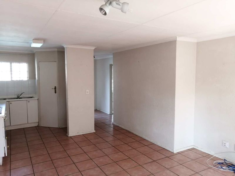 An empty open-plan living and kitchen area featuring tiled flooring, neutral walls, and basic kitchen cabinetry, offering a blank canvas for renovation.
