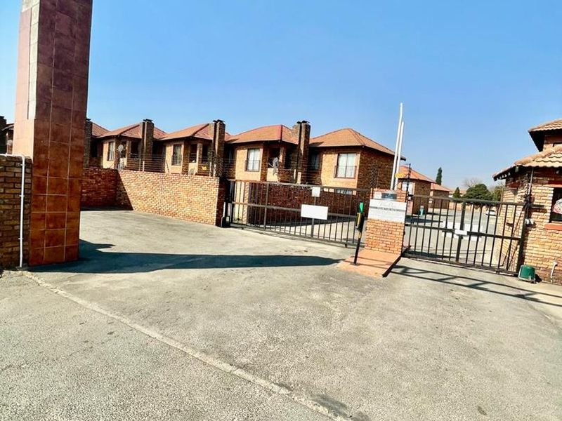 Front entrance view of the cluster complex featuring a secure gated access point, brick boundary walls, and paved driveway.