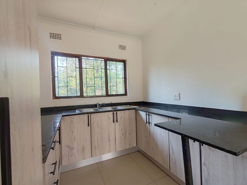 A clean, functional kitchen featuring light wood-look cabinetry, dark granite countertops, a double sink, and a breakfast bar, offering a neutral base for customization.