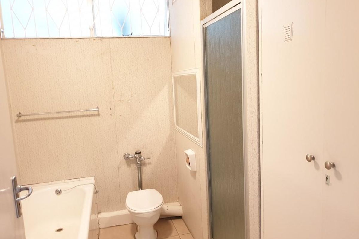 A dated bathroom featuring a bathtub, separate shower enclosure, and built-in storage cupboard, requiring cosmetic updates to modernize the space.