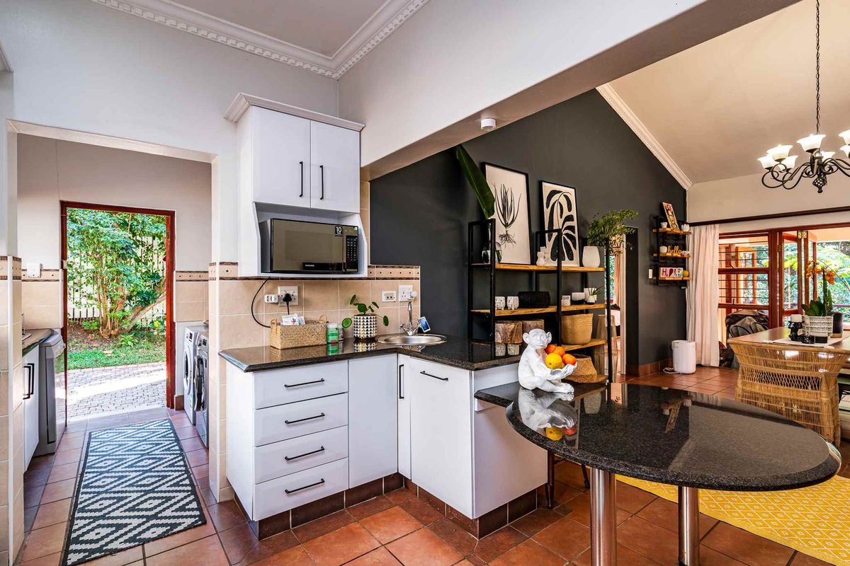 A functional kitchen area featuring granite countertops, white cabinetry, and a built-in microwave, with an adjacent laundry space and access to the garden.