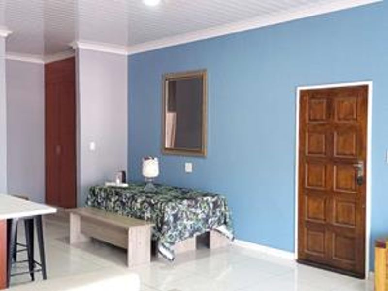 Open plan living area featuring tiled flooring, a panelled ceiling, and a solid wood entrance door with built-in storage cupboards.