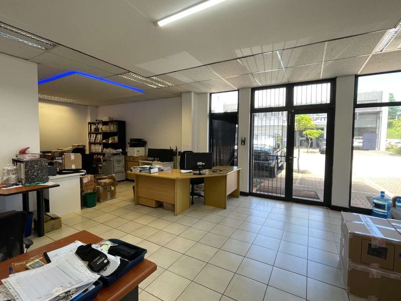 Functional office space featuring ceramic tiled flooring, suspended ceiling with integrated lighting, and large glass doors providing natural light and street access.