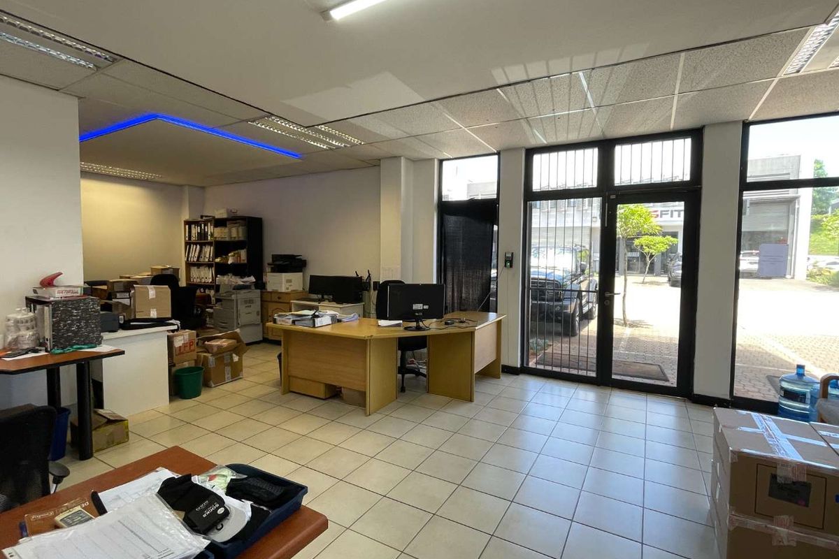 Functional office space featuring ceramic tiled flooring, suspended ceiling with integrated lighting, and large glass doors providing natural light and street access.