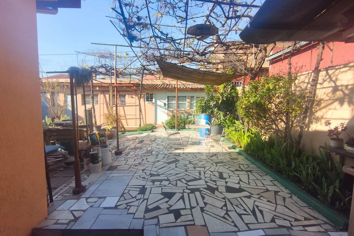 A rear courtyard area featuring paved flooring, a metal trellis structure, and boundary walls, offering potential for outdoor living space improvement.