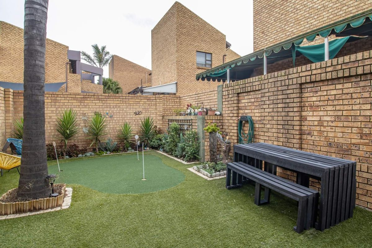 A private rear courtyard featuring a low-maintenance artificial grass putting green, enclosed by face-brick boundary walls and a retractable awning.