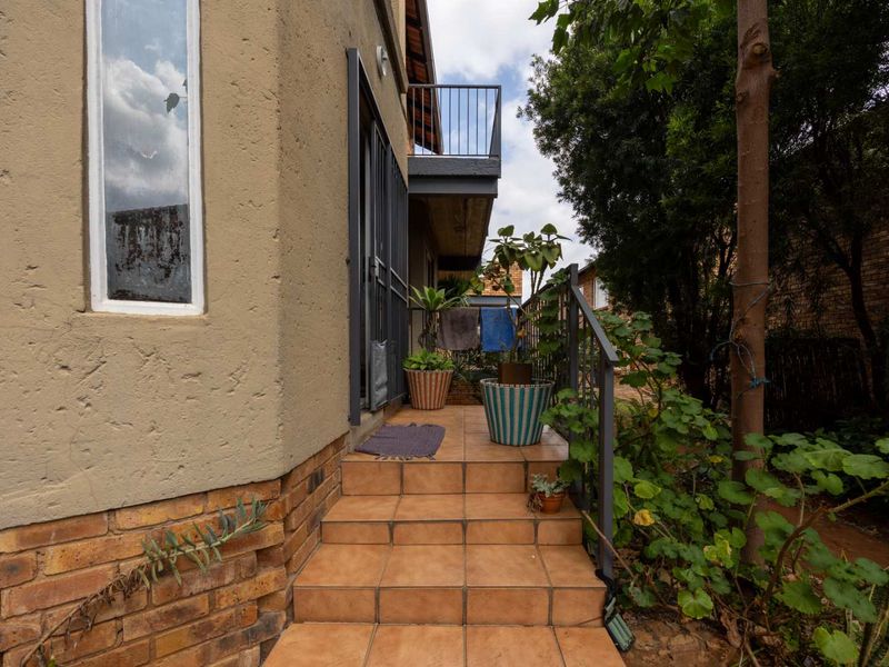 Rear exterior view of the townhouse featuring a tiled staircase, metal security gate, and an upper-level balcony with metal railing.