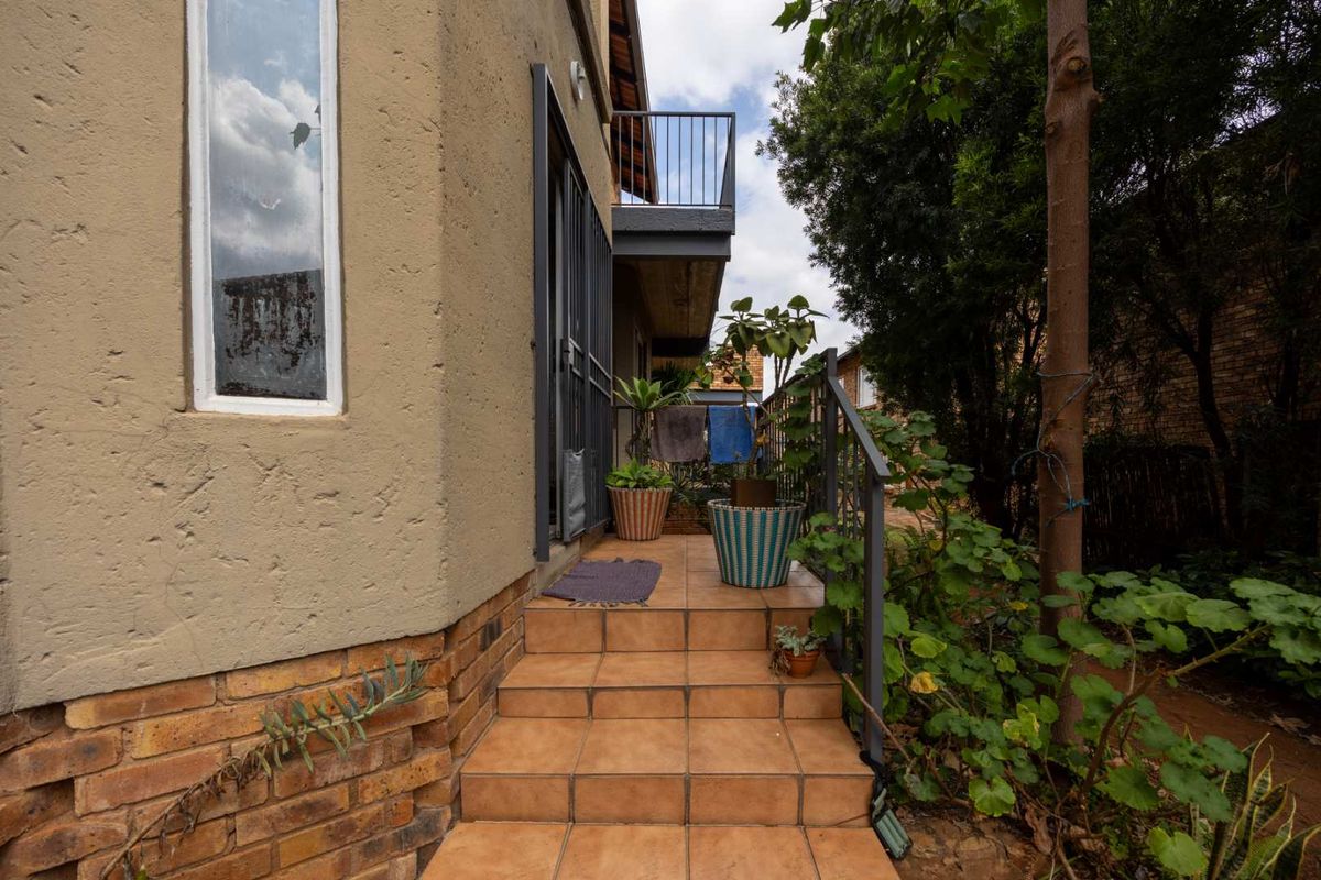 Rear exterior view of the townhouse featuring a tiled staircase, metal security gate, and an upper-level balcony with metal railing.