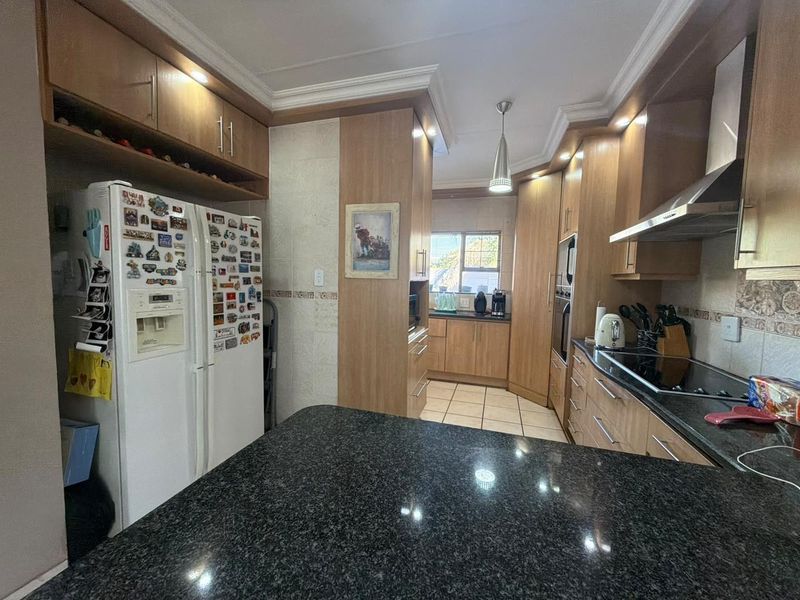 A functional kitchen featuring granite countertops, extensive wooden cabinetry, built-in oven, and hob, with tiled flooring and coved ceiling details.