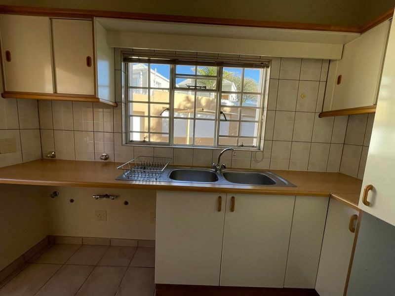 A functional kitchen area featuring a double bowl sink, tiled splashback, and ample built-in cabinetry, ready for a modern update.